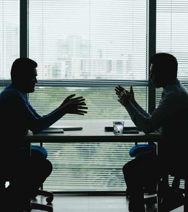 Silhouettes of business people sitting at table against the office window and discussing various issues